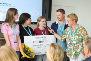 Five people on a stage presenting a large €350 prize check to a student speaker, with a bouquet in the foreground