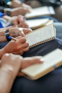 Close-up of hands taking notes in a spiral notebook with a blue pen.